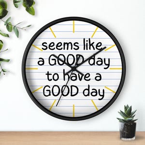 May include: A round wall clock with a black frame. The clock face has a white background with blue lines and yellow markers. The text "seems like a GOOD day to have a GOOD day" is printed in black.