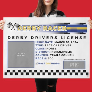 May include: A white and blue derby racer license with the text "DERBY RACER" and "DERBY DRIVERS LICENSE". The license includes the issue date, type, class, district, council, race number, and a blue and gold member checkmark. The license has cut-out areas for a photo and a registered derby car.