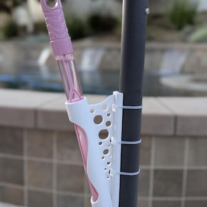 May include: White plastic holder with holes for a pink bubble wand attached to a black pole with white ties.