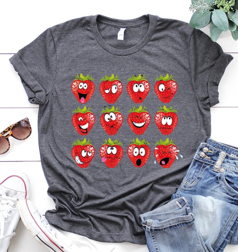 May include: A gray t-shirt with a graphic of 12 strawberries with different facial expressions. The strawberries are red with green leaves.