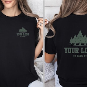 Puede incluir: Camiseta negra con un gr&aacute;fico de bosque y el texto "YOUR LOGO" en verde. El dise&ntilde;o se repite en la parte delantera y trasera de la camiseta. La camiseta tiene mangas cortas y cuello redondo.