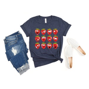 May include: A navy blue t-shirt with a graphic of 12 red strawberries with different facial expressions.