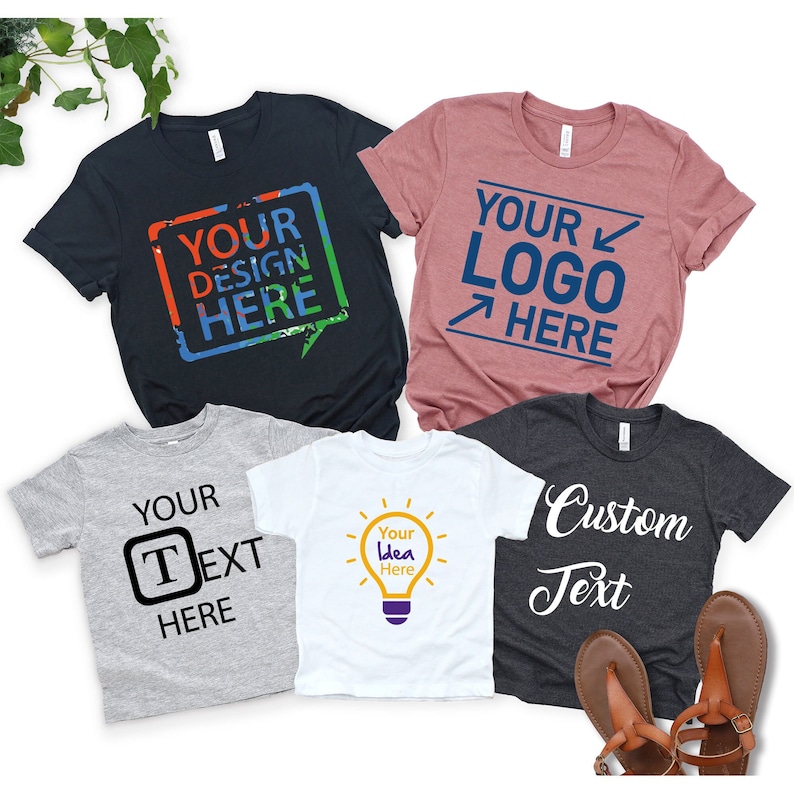 May include: Five different t-shirts with customizable designs. The shirts are in various colors, including black, gray, white, and pink. The designs include text, a lightbulb, and a logo. The text on the shirts reads "Your Design Here", "Your Logo Here", "Your Text Here", "Your Idea Here", and "Custom Text".