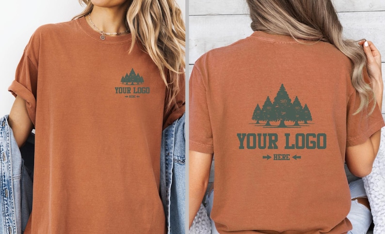 Puede incluir: Camiseta de color &oacute;xido con un gr&aacute;fico de bosque y el texto "YOUR LOGO HERE". El dise&ntilde;o se repite en la parte delantera y trasera. La camiseta tiene mangas cortas y un corte holgado.