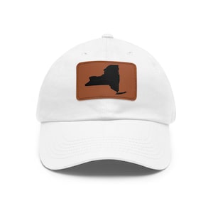 Könnte beinhalten: Eine weiße Baseballkappe mit einem rechteckigen, braunen Lederaufnäher in der Mitte der Vorderseite. Der Aufnäher zeigt eine einfarbige schwarze Silhouette des Bundesstaates New York. Die Kappe hat einen gebogenen Schirm und eine Krone.