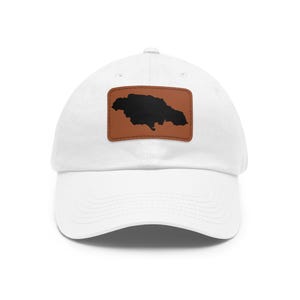 Può includere: Un cappellino da baseball bianco con una toppa rettangolare in pelle marrone sulla parte anteriore. La toppa mostra una sagoma nera solida dell'isola della Giamaica, centrata sulla corona sopra la visiera curva del cappellino.