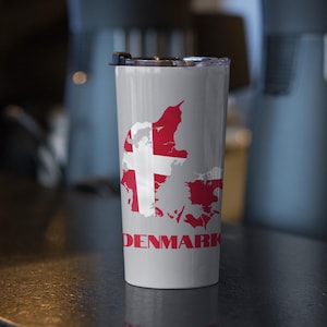 Könnte beinhalten: Eine graue Reise-Thermoskanne mit einer weißen Umrandung von Dänemark und der dänischen Flagge in Rot und Weiß. Das Wort "DENMARK" ist in Rot unterhalb der Umrandung aufgedruckt.