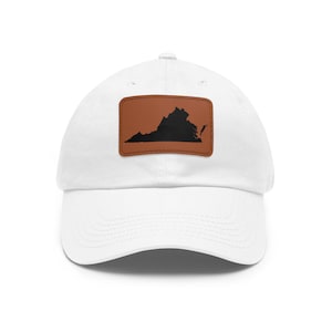 May include: A white baseball cap featuring a rectangular brown leather patch centered on the front. The patch displays a black silhouette of the state of Virginia. The cap has a curved brim and stitched detailing across the crown and visor.