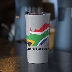 Könnte beinhalten: Ein grauer Edelstahlbecher mit einer weißen Umrandung der Karte von Südafrika und den Farben der südafrikanischen Flagge. Der Text "SOUTH AFRICA" ist in Schwarz unter der Karte aufgedruckt.