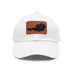 May include: A white baseball cap featuring a rectangular brown patch on the front. The patch displays a solid black silhouette of the country of Austria centered on the brown background. The cap has a curved brim and a structured crown design.