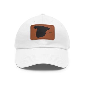 May include: A white baseball cap featuring a rectangular brown patch on the front. The patch displays a solid black silhouette map of Spain centered on the material. The cap has a curved brim and a structured crown with stitched eyelets.