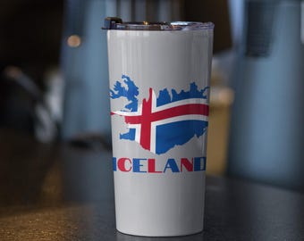 Könnte beinhalten: Ein weißer Reisebecher mit der Karte von Island in Blau, einem roten Kreuz und dem Wort "ICELAND" in Blau und Rot. Der Becher hat einen schwarzen Deckel. Das Design ist eine patriotische Darstellung Islands.