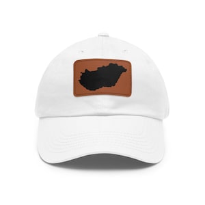 May include: A white baseball cap featuring a rectangular brown patch on the front. The patch displays a solid black silhouette of the country of Hungary. The cap has a curved brim and a structured crown with stitched eyelets for ventilation.