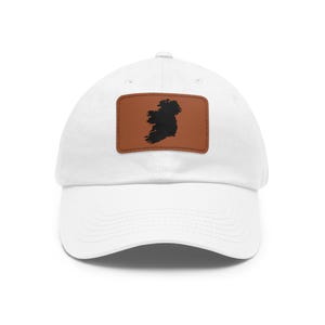 May include: A white baseball cap featuring a rectangular brown patch centered on the front. The patch displays a black silhouette of the island of Ireland. The cap has a structured crown, a curved brim, and stitched eyelets for ventilation.