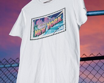 May include: White t-shirt with a vintage-style postcard graphic featuring the Statue of Liberty and the text "Greetings from NEW YORK".