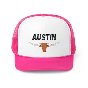 May include: A pink and white trucker hat with a black and white graphic of a longhorn steer and the word "AUSTIN" on the front.