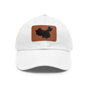 Può includere: Un cappellino da baseball bianco con una toppa rettangolare marrone centrata sulla parte anteriore. La toppa mostra una sagoma nera solida della mappa della Cina. Il cappellino presenta una visiera curva e una corona strutturata.