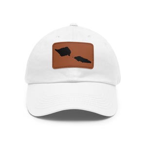 May include: A white baseball cap featuring a rectangular brown leather patch centered on the front. The patch displays a black silhouette graphic of the islands of Samoa, including Savai'i and Upolu, with visible stitching around the patch edges.