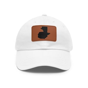 May include: A white baseball cap featuring a rectangular brown leather patch centered on the front. The patch displays a solid black silhouette of the country of Guatemala. The cap has a curved brim and a structured crown with stitched eyelets.