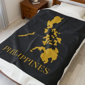 Puede incluir: Una manta negra con un contorno dorado de Filipinas y la palabra "FILIPINAS" en letras doradas.