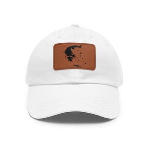Puede incluir: Una gorra de béisbol blanca con un parche rectangular marrón centrado en la parte delantera. El parche muestra una silueta negra del mapa de Grecia. La gorra tiene una visera curva y una corona estructurada con ojales cosidos.