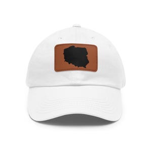 May include: A white baseball cap featuring a rectangular brown leather patch centered on the front. The patch displays a solid black silhouette of the map of Poland. The cap has a curved brim and a structured crown with stitched eyelets.