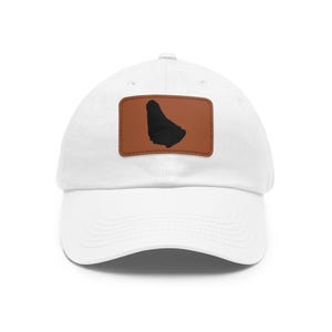 May include: A white baseball cap featuring a rectangular brown leather patch on the front. The patch displays a black silhouette of the island of Barbados. The cap has a curved brim and a structured crown with stitched eyelets for ventilation.
