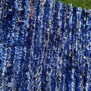 Puede incluir: Una alfombra azul y blanca peluda con un diseño tejido texturizado. La alfombra tiene una forma rectangular larga y está hecha de fibras suaves y esponjosas.