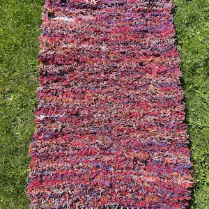 Puede incluir: Una alfombra colorida tejida a mano con una textura peluda. La alfombra está hecha con una variedad de colores, incluyendo rojo, naranja, amarillo, azul y morado. La alfombra tiene un borde de flecos.