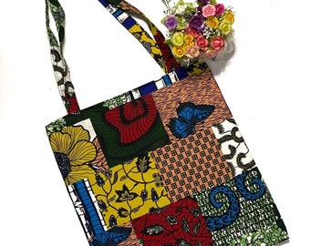 Pode incluir: Uma bolsa tote colorida com um design de patchwork que apresenta borboletas, flores e padrões geométricos. A bolsa tem duas alças longas e é feita de tecido.