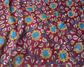 May include: A maroon fabric with a floral pattern featuring blue, yellow, and white flowers on a burgundy background. The fabric has a cream-coloured border.