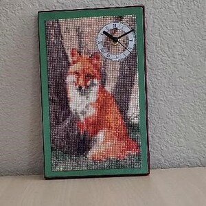 Könnte beinhalten: Ein gerahmtes Kreuzstich-Kunstwerk mit einem roten Fuchs, der in einer Waldlandschaft sitzt. Das Kunstwerk enthält ein Zifferblatt mit römischen Ziffern.