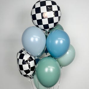 Puede incluir: Un grupo de globos en tonos de azul, verde y blanco. Dos globos tienen un patr&oacute;n de cuadros blancos y negros. Los otros globos son de colores lisos, incluyendo azul claro, verde azulado y verde salvia. Se adjuntan cintas plateadas.