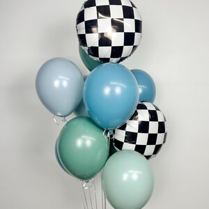 Puede incluir: Un conjunto de globos en varios tonos de azul, verde y blanco. Dos globos tienen un patr&oacute;n de cuadros blancos y negros. Los otros globos son de colores lisos. Los globos est&aacute;n atados con cintas transparentes.