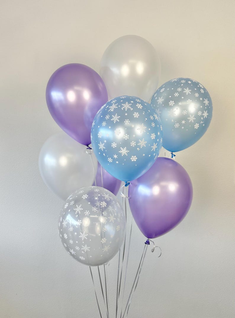 Puede incluir: Un mont&oacute;n de globos en blanco, azul claro y morado con patrones de copos de nieve. Los globos est&aacute;n atados juntos y listos para una fiesta.