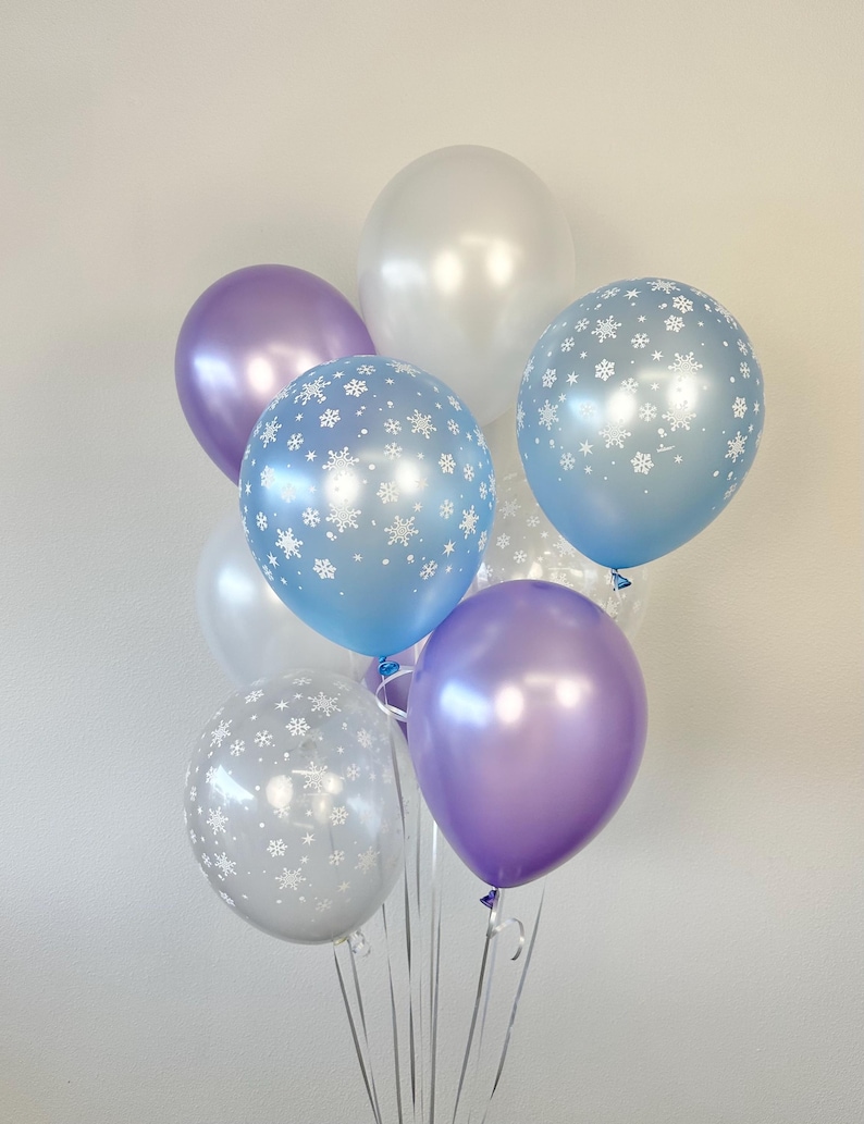 Puede incluir: Un ramo de globos en varios tonos de azul y morado con patrones de copos de nieve. Los globos est&aacute;n atados juntos con una cinta transparente.