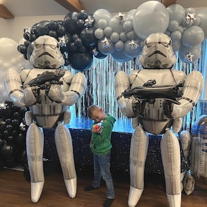 Pu&ograve; includere: Due grandi palloncini gonfiabili a forma di Stormtrooper in piedi, ognuno dei quali impugna un blaster nero. Un arco di palloncini nei toni del bianco, grigio e nero con accenti a stella argentati &egrave; posizionato dietro, accanto a un palloncino R2-D2.