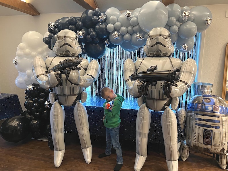 Pu&ograve; includere: Due grandi palloncini gonfiabili a forma di Stormtrooper in piedi, ognuno dei quali impugna un blaster nero. Un arco di palloncini nei toni del bianco, grigio e nero con accenti a stella argentati &egrave; posizionato dietro, accanto a un palloncino R2-D2.