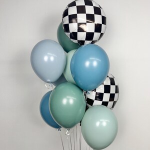 Puede incluir: Un conjunto de globos en tonos azules y verdes, con dos globos a cuadros blancos y negros. Los globos est&aacute;n atados con cintas plateadas, creando un arreglo festivo.