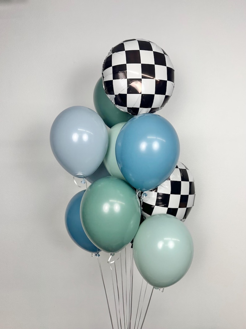 Puede incluir: Un conjunto de globos en tonos azules y verdes, con dos globos a cuadros blancos y negros. Los globos est&aacute;n atados con cintas plateadas, creando un arreglo festivo.