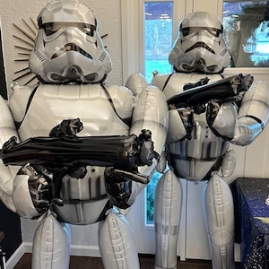 Pu&ograve; includere: Due grandi figure gonfiabili di Stormtrooper realizzate in materiale bianco e grigio lucido. Ogni figura indossa un casco e un'armatura dettagliati, tenendo in mano un fucile blaster di plastica nera. Le figure sono in piedi, imitando l'iconico aspetto del soldato.