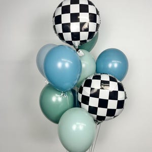 Puede incluir: Un ramo de globos en tonos azules y verdes, con dos globos redondos a cuadros blancos y negros. Los globos est&aacute;n atados con cinta plateada, creando un arreglo festivo.