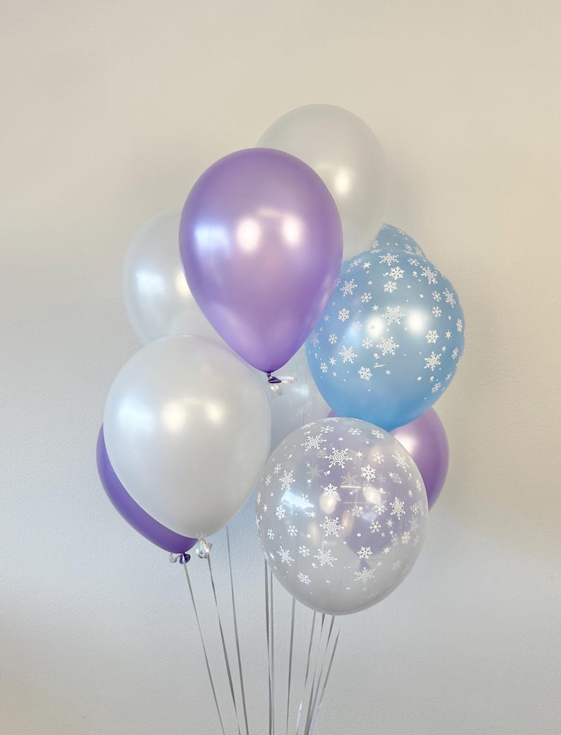 Puede incluir: Un mont&oacute;n de globos en blanco, azul claro y morado. Algunos de los globos tienen un patr&oacute;n de copo de nieve.
