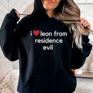 Może przedstawiać: Czarna bluza z kapturem z białym nadrukiem "i ♥ leon from residence evil".