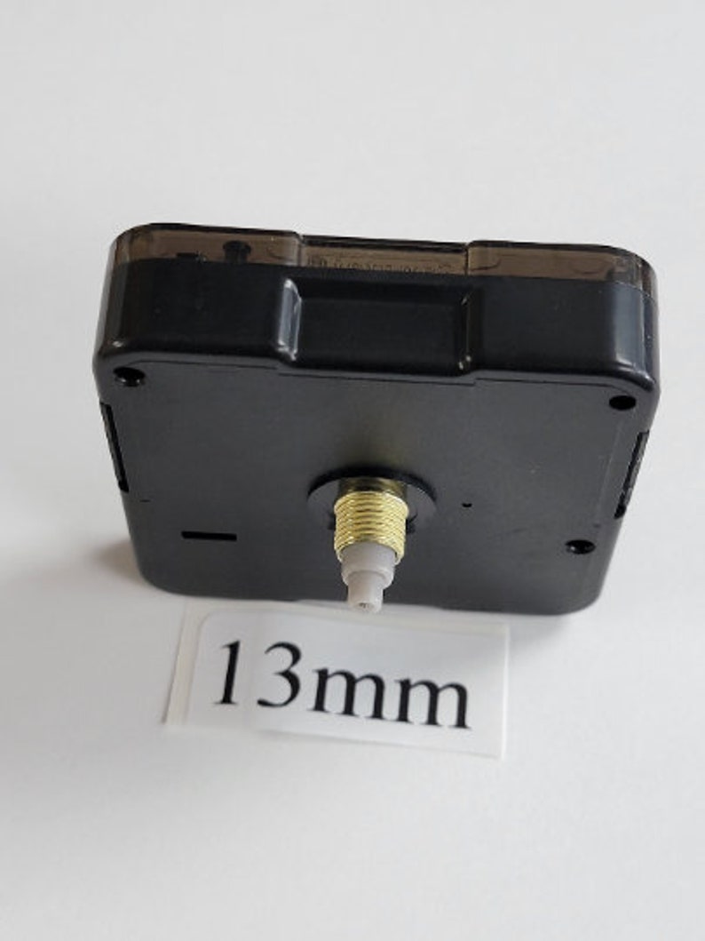 K&ouml;nnte beinhalten: Schwarzes Uhrwerk mit einer 13 mm Welle. Das Uhrwerk hat eine transparente Kunststoffabdeckung und eine goldfarbene Welle.