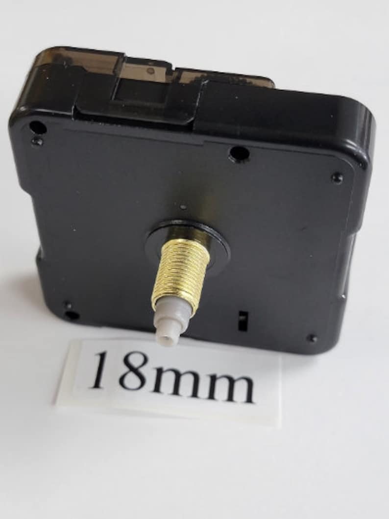 K&ouml;nnte beinhalten: Schwarzes Uhrwerk mit einer goldfarbenen Welle und einer wei&szlig;en Kunststoffspitze. Die Welle ist 18 mm lang.