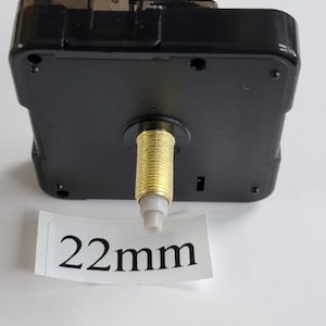 K&ouml;nnte beinhalten: Ein schwarzes Uhrwerk mit einer goldfarbenen Welle und einer wei&szlig;en Kunststoffspitze. Das Uhrwerk hat einen Durchmesser von 22 mm.