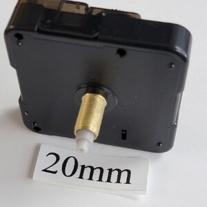 K&ouml;nnte beinhalten: Schwarzes Uhrwerk mit einer goldfarbenen Welle und einem wei&szlig;en Etikett mit der Aufschrift "20 mm".