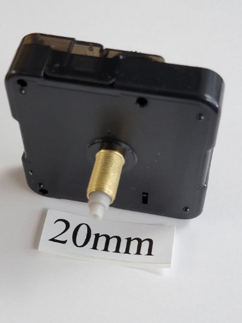 K&ouml;nnte beinhalten: Schwarzes Uhrwerk mit einer goldfarbenen Welle und einem wei&szlig;en Etikett mit der Aufschrift "20 mm".