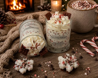 May include: Two glass candles with white wax, topped with whipped wax, chocolate bar pieces, and red sprinkles. The labels read Wax & Wix Bakery, Peppermint Mocha, Net Wt 13 oz. Two white snowflake-shaped wax melts and chocolate chips are nearby.